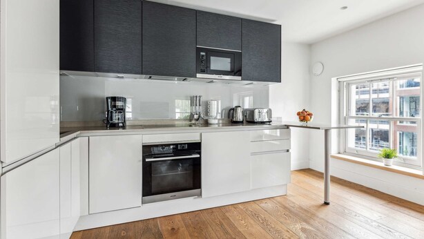A modern kitchen with white cabinetry, a built-in oven, a microwave, and a coffee maker.