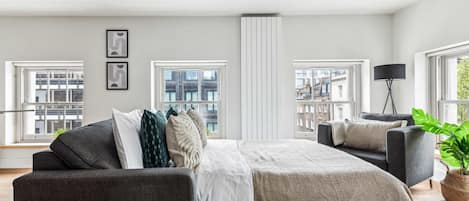 Een ruime slaapkamer met een groot bed, twee zithoeken en meerdere ramen met uitzicht op de stad.