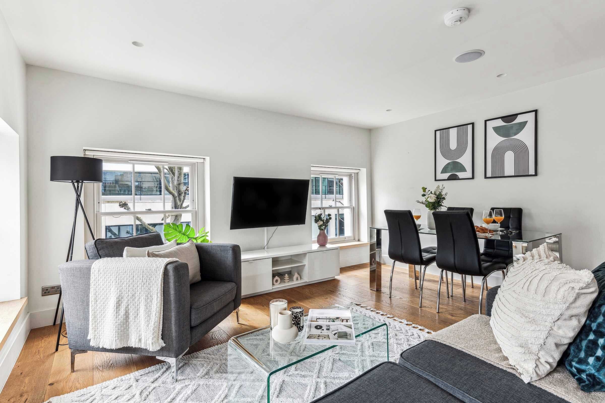 A modern living room with a flat-screen TV, a sofa, a coffee table, and a dining area with chairs and a table.