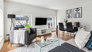 A modern living room with a flat-screen TV, a sofa, a coffee table, and a dining area with chairs and a table.