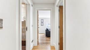 A hallway with a wooden floor, white walls, and a door leading to a room with a grey sofa.