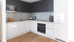 Una cocina moderna con armarios blancos, microondas, fregadero, cafetera y horno.
