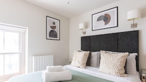 Una habitación de hotel moderna con una cama grande, dos lámparas fijadas a la pared y obras de arte enmarcadas.