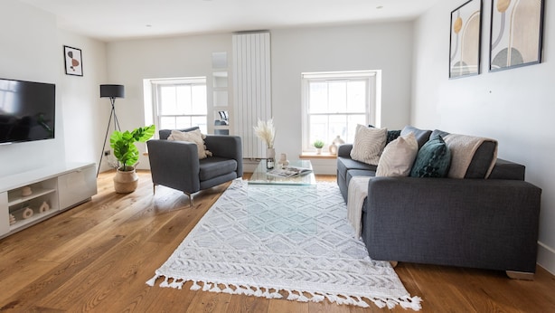 Una sala de estar moderna con un sofá gris, una mesa de centro blanca y un tapete grande de color blanco.