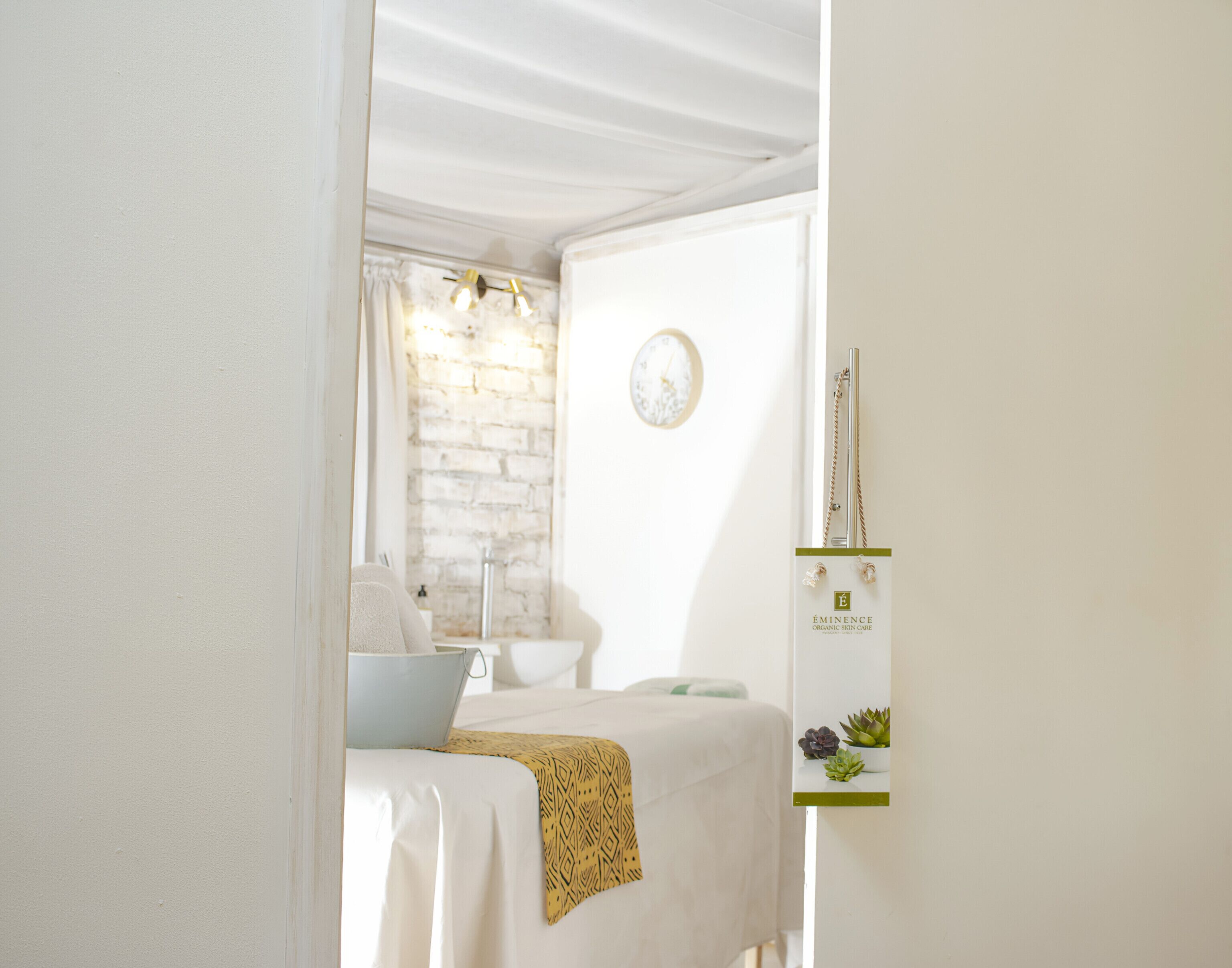 Ein Hotelzimmer mit einem Bett, einem kleinen Tisch, einer Wanduhr und einem an der Wand befestigten Regal mit einer Pflanze.