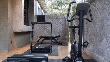 Área de ginástica coberta ao ar livre com equipamentos de exercício, incluindo esteira, elíptico e máquinas de peso.