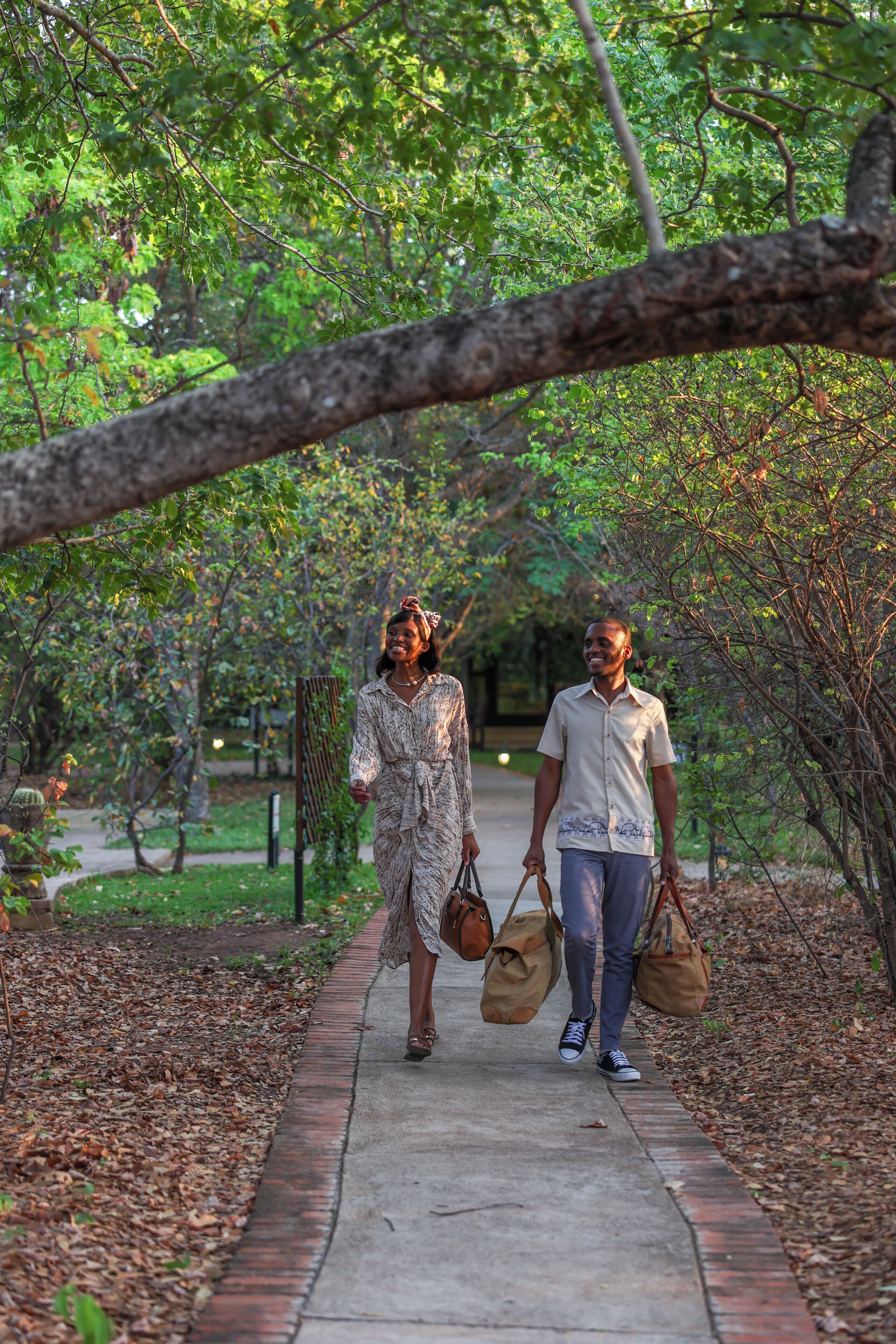 Two people walking on a paved path surrounded by trees and greenery.