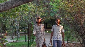 Two people walking on a paved path surrounded by trees and greenery.