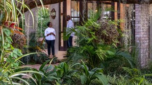 Un jardín exuberante con un arco de madera que da acceso a la entrada de un edificio.