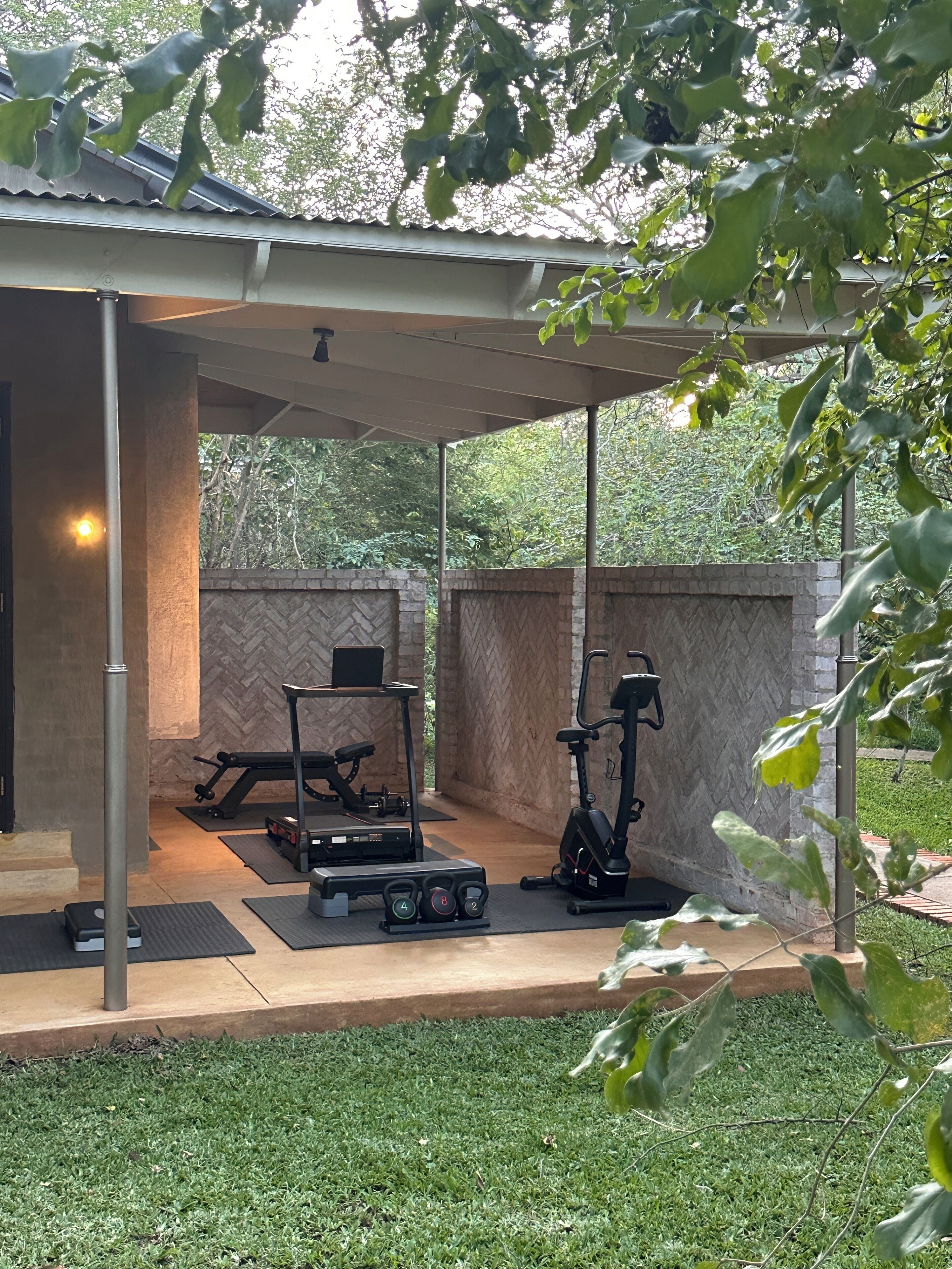 Un espace de remise en forme en plein air équipé d’appareils d’exercice, un espace de repos couvert et un mur en pierre servant de décor.