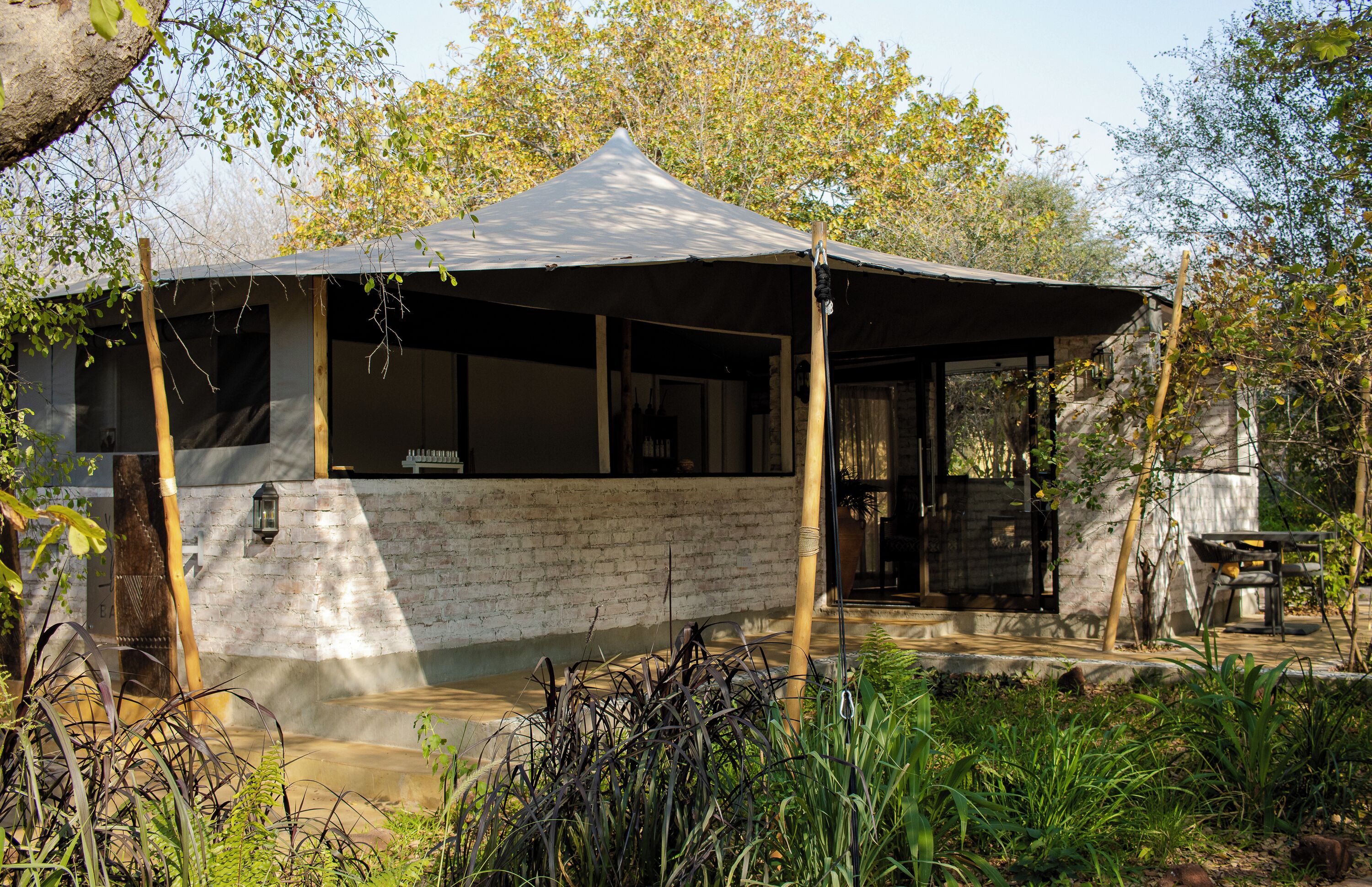 A rustic cabin with a large canopy, brick walls, and a wooden deck.