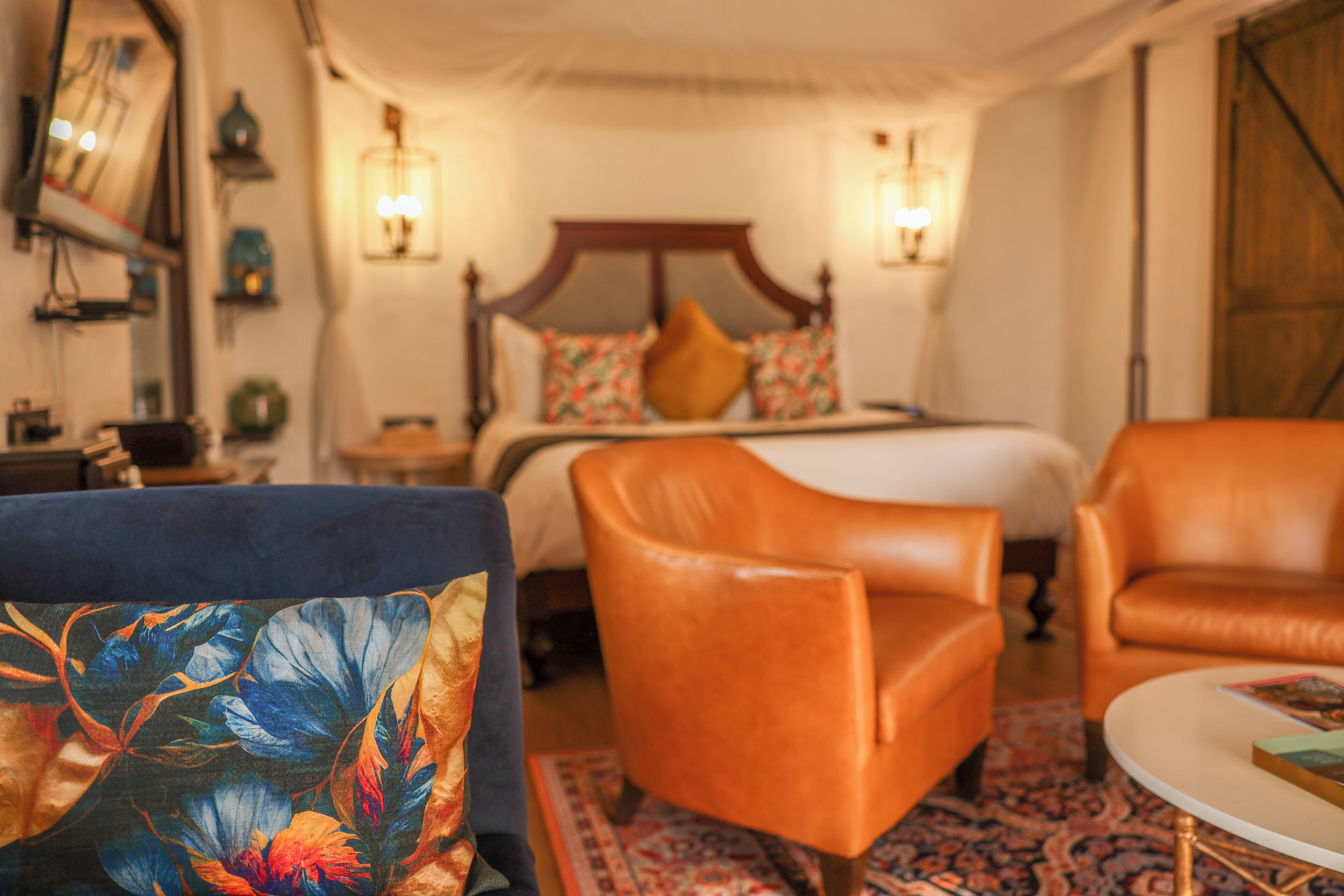 Un dormitorio con cama, dos sillas, una mesita de noche y una lámpara.