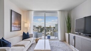 Una sala de estar moderna con un sofá, una mesita de centro, un televisor y un ventanal con vistas a la ciudad.
