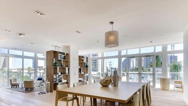 Un comedor espacioso con una larga mesa de madera y sillas, rodeado de grandes ventanales con vistas a la ciudad.