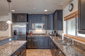 A modern kitchen with dark cabinetry, granite countertops, stainless steel appliances, and a large window. - Luge Lane 5 Bedroom Townhouse by RedAwning (Park City)