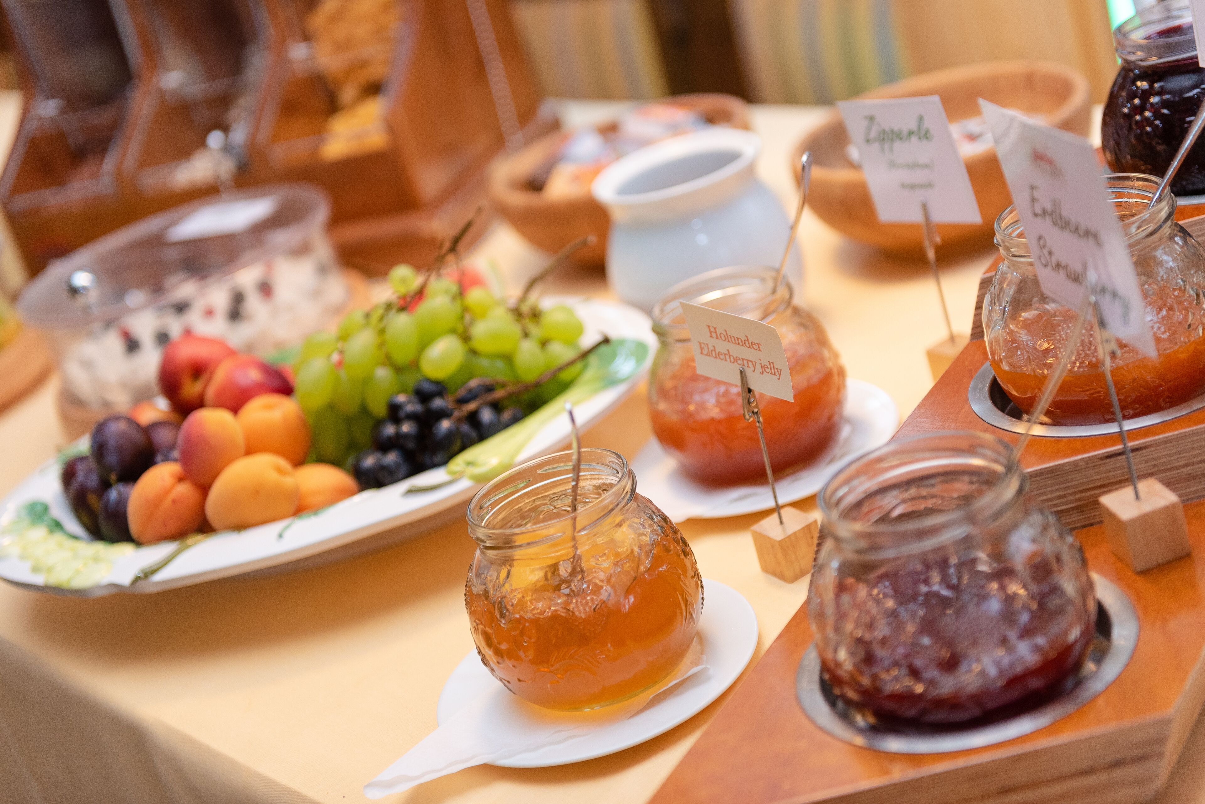 En buffetbod med forskellige spisemuligheder, herunder frugt, marmelade og honning.