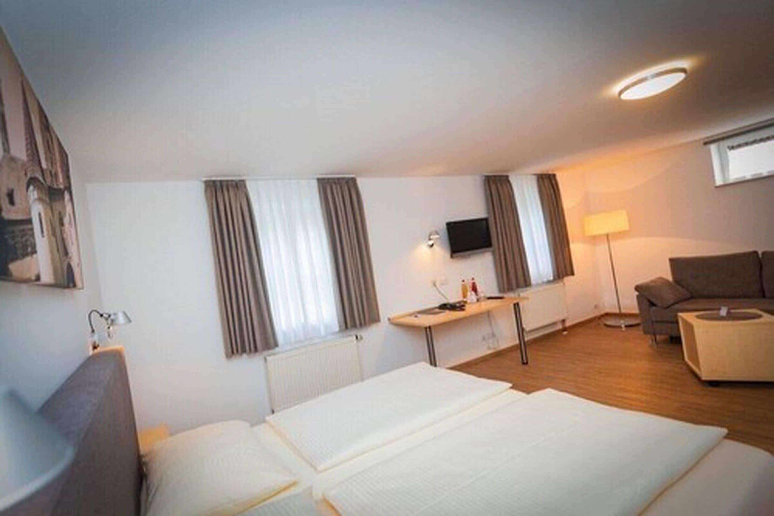 A hotel room with a bed, a desk, a TV, a sofa, and a lamp.