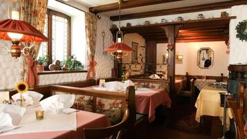 Un restaurante acogedor con vigas de madera, papel tapiz floral y mesas dispuestas para comer.