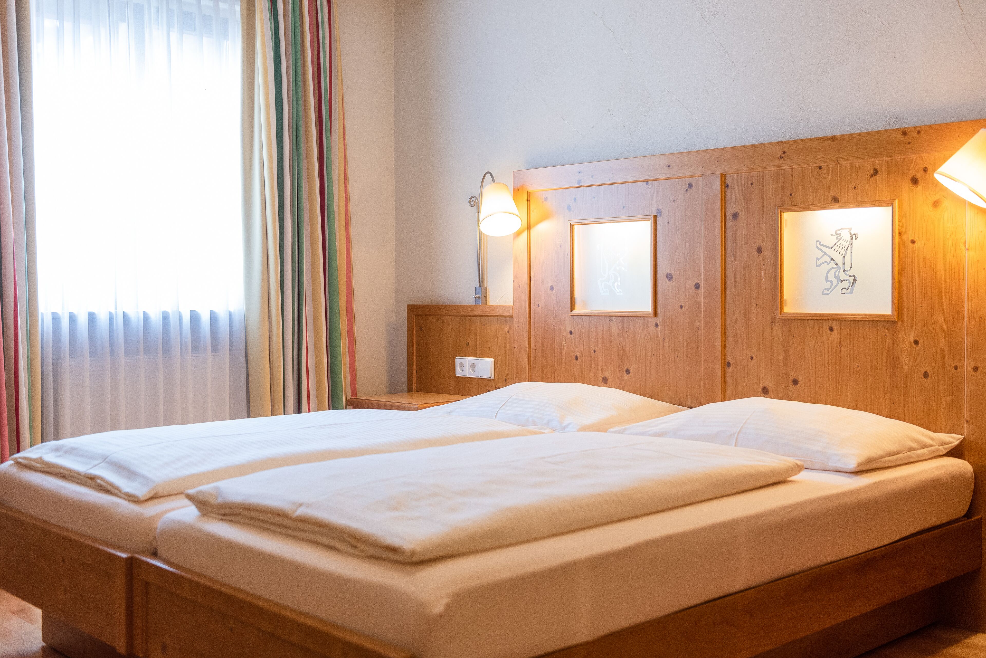 A double bed with a wooden headboard, two bedside tables, and a window with curtains.