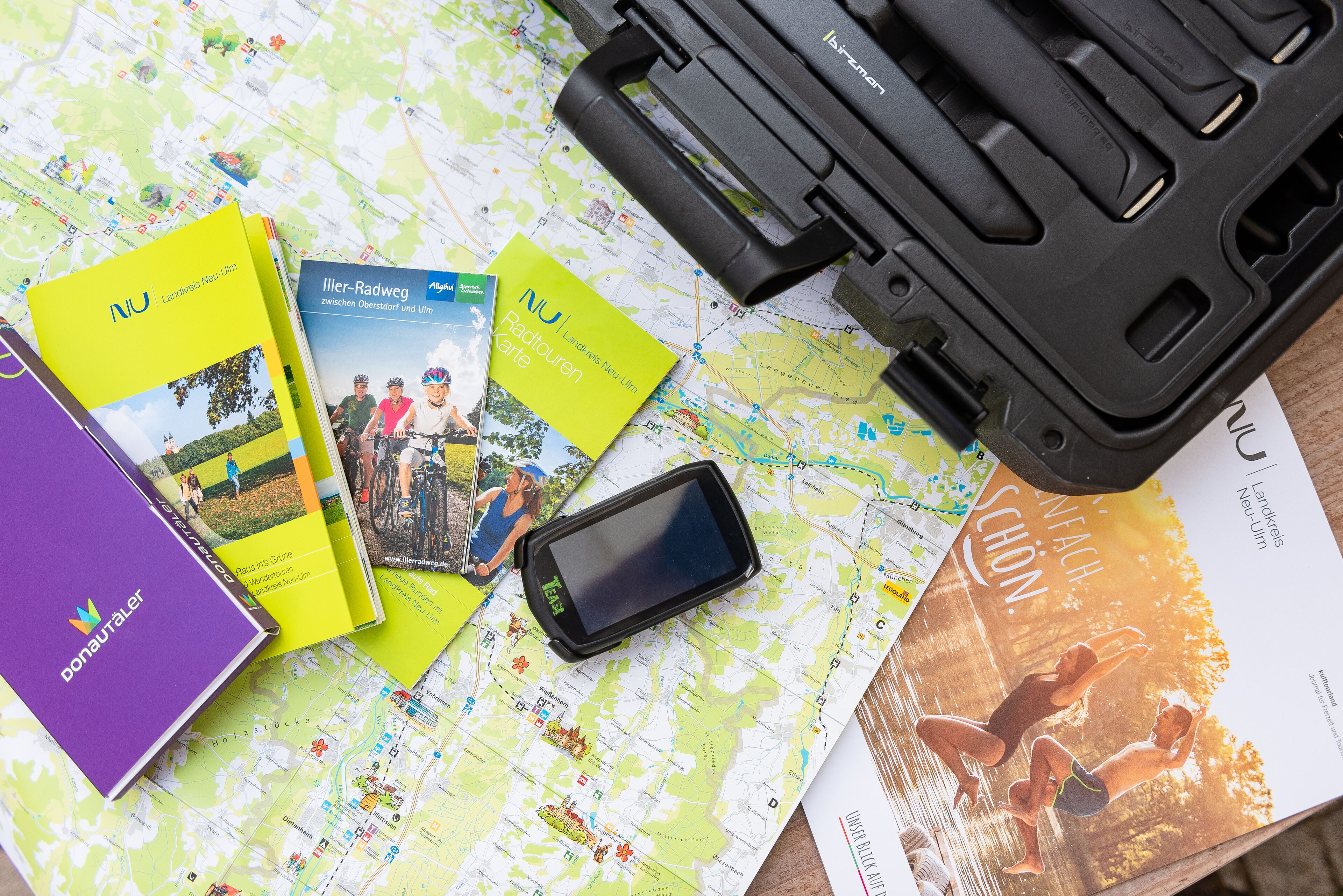 A map, travel brochures, a smartphone, and a black case on a table.
