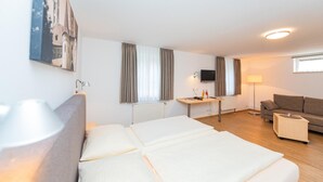 Een hotelkamer met een bed, bureau, televisie, bank en een schilderij aan de muur.