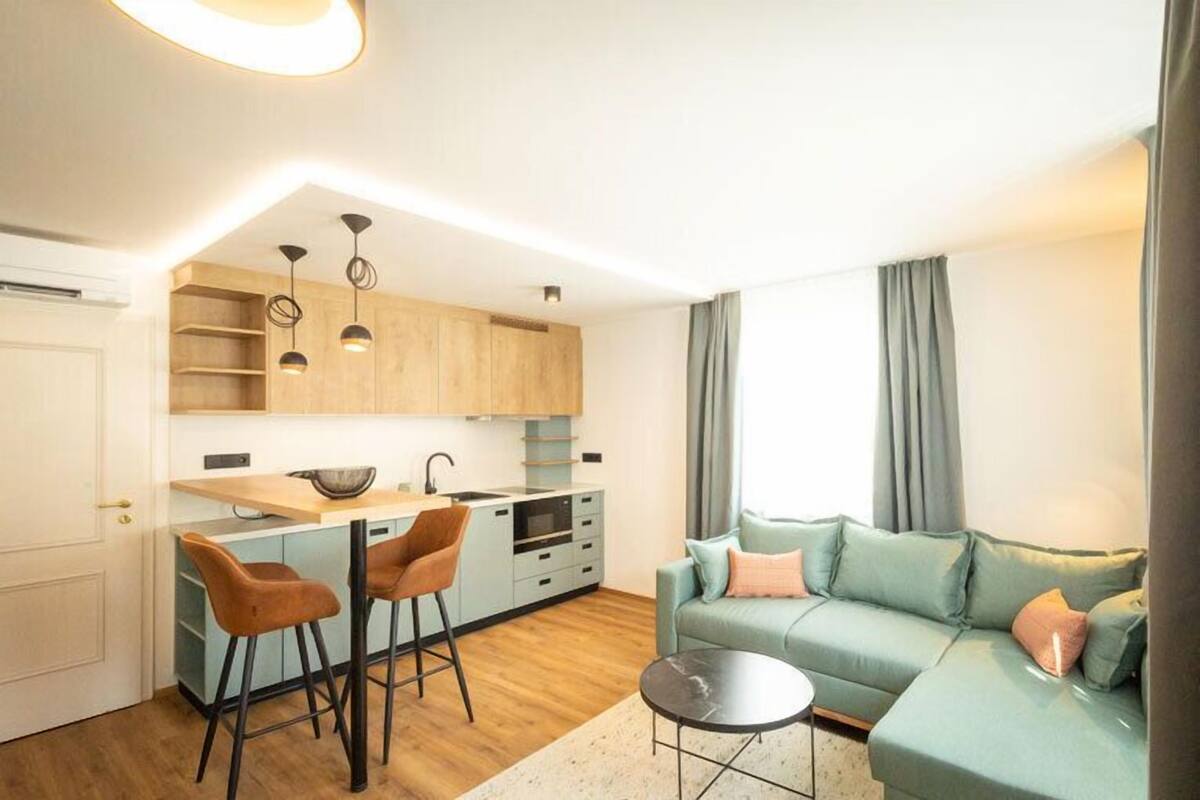 Een modern appartement met een keuken, een eethoek met barstoelen, een woonkamer met een bank en een kleine ronde tafel.