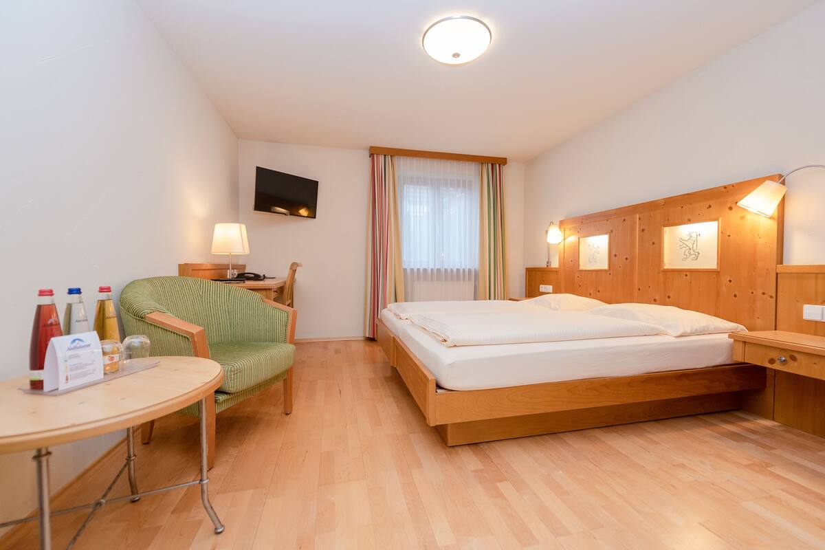 Een hotelkamer met een houten bed, een bureau met stoel, een aan de muur bevestigde televisie en een raam met gordijnen.
