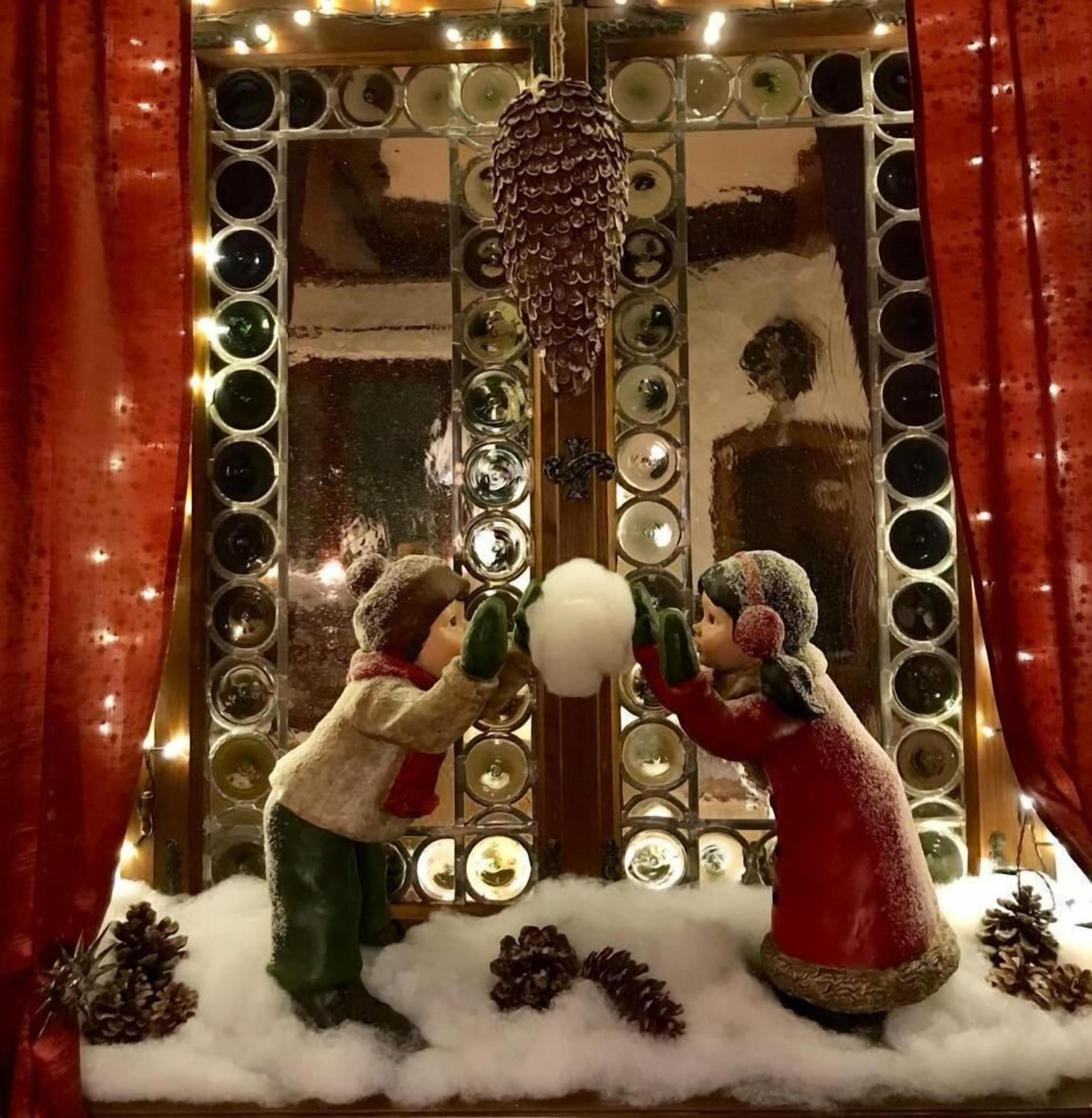 Duas figuras vestidas para o inverno, sobre uma superfície coberta de neve com piões, em frente a um espelho decorativo com molduras circulares.