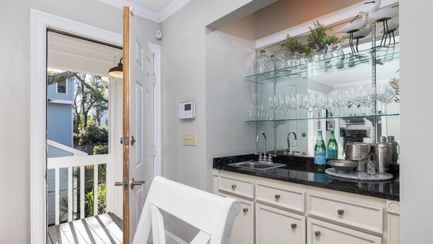 A kitchen with a glass-fronted cabinet displaying wine glasses and bottles, a sink, and a door leading to a balcony. - Stay @ Here Comes the Sun on Isle of Palms (Isle of Palms)