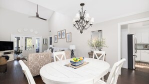 A spacious living room with a white dining table, white chairs, a chandelier, and a ceiling fan. - Stay @ Here Comes the Sun on Isle of Palms (Isle of Palms)
