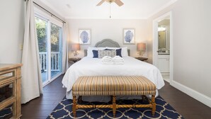 A bedroom with a large bed, a ceiling fan, a bench, and a view of the outdoors. - Stay @ Here Comes the Sun on Isle of Palms (Isle of Palms)