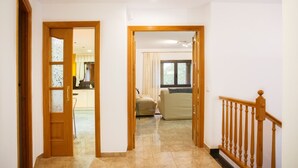 A hallway with a wooden door leading to a kitchen and a living area with a sofa. - House with private pool, isolated and very quiet at the end of town. (Llampaies)