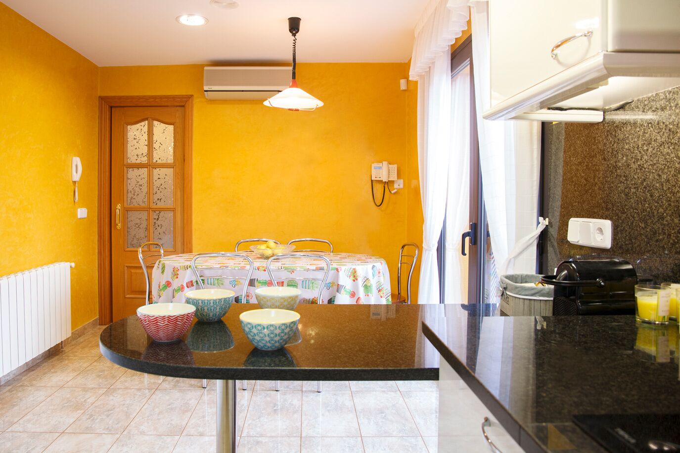 A kitchen with a dining table set for four, a coffee machine, and a refrigerator.
