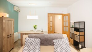 A modern living room with a sofa, two patterned cushions, a wooden cabinet, a dining table with chairs, and a kitchen area visible through an open door. - House with private pool, isolated and very quiet at the end of town. (Llampaies)
