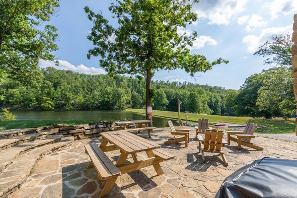 An outdoor patio with picnic tables and chairs, a stone floor, and a view of a lake and forest. - YOUR OWN PRIVATE 12 ACRE LAKE, 80 ACRES, HOT TUB & GAME BARN (Columbus)
