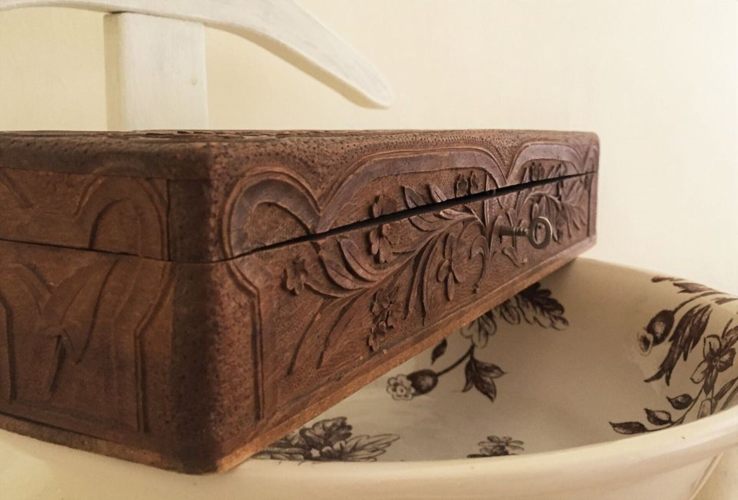 Une boîte en bois ornée de motifs floraux et portant le chiffre « 6 », posée sur une surface blanche à motifs floraux.