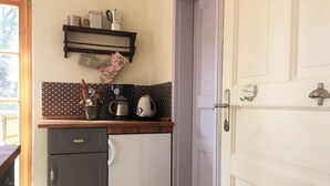Pieni, käytännöllinen keittiö, jossa on jääkaappi, kahvinkeitin ja vedenkeitin työtasolla.
