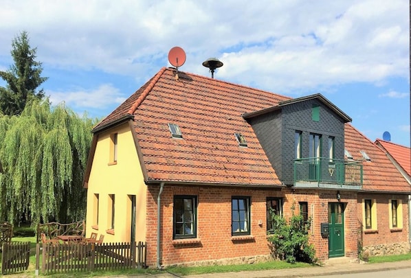 A two-story house with a red-tiled roof, a satellite dish, and a small balcony.