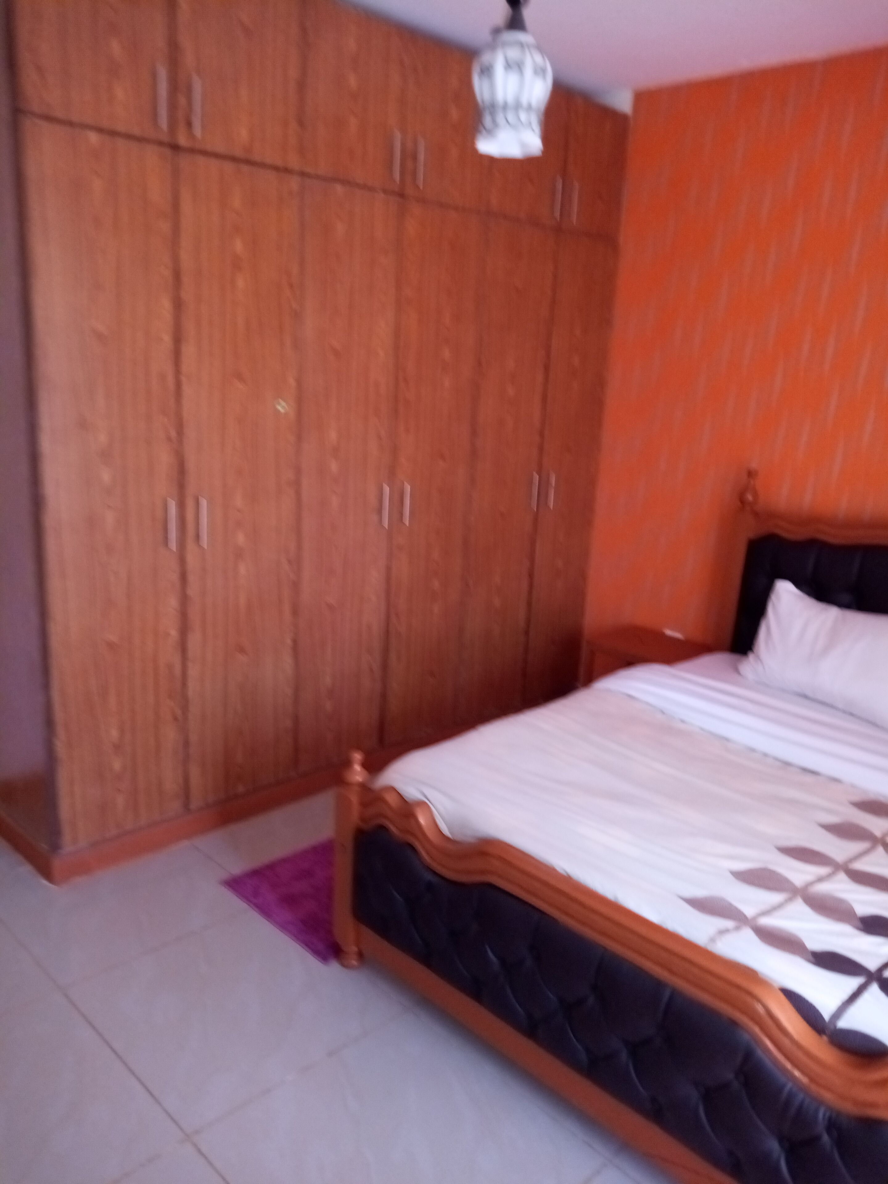 Un dormitorio con cama, armario de madera y lámpara colgante.