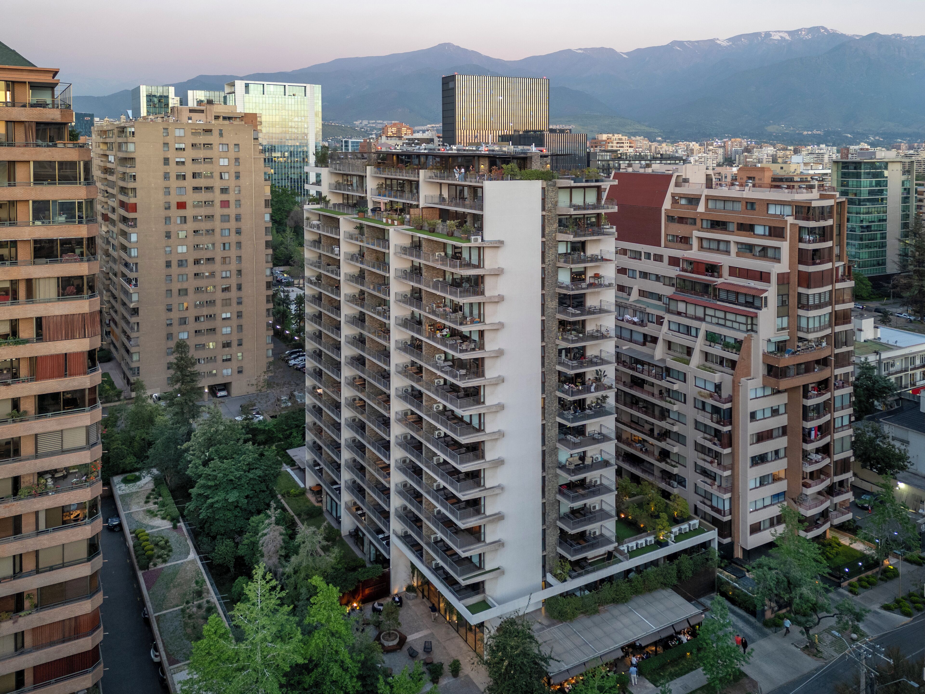A high-rise building with multiple balconies, a rooftop garden, and a view of surrounding urban area and mountains.