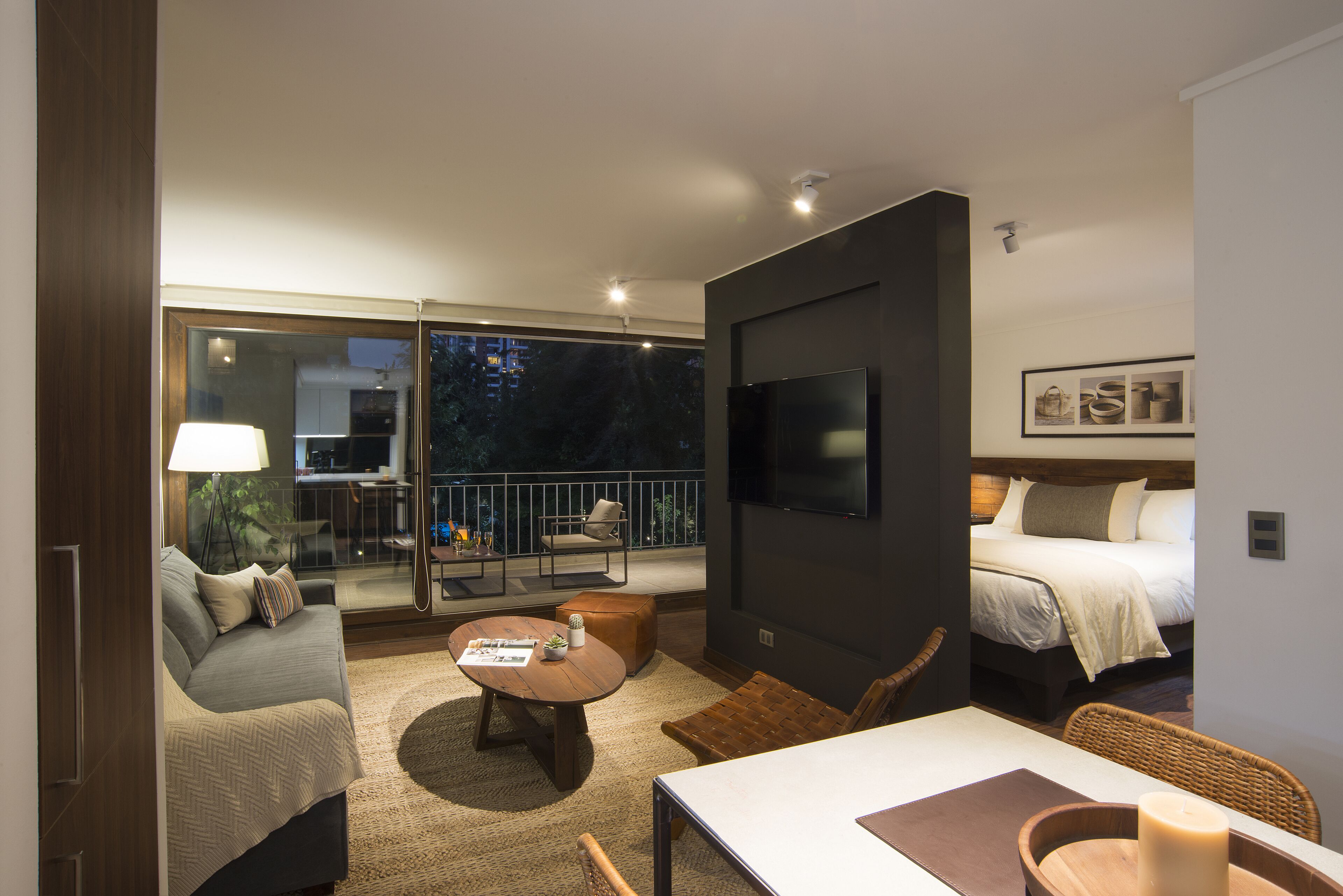 Una habitación de hotel moderna con balcón, televisión de pantalla plana, cama, sofá y zona de comedor.