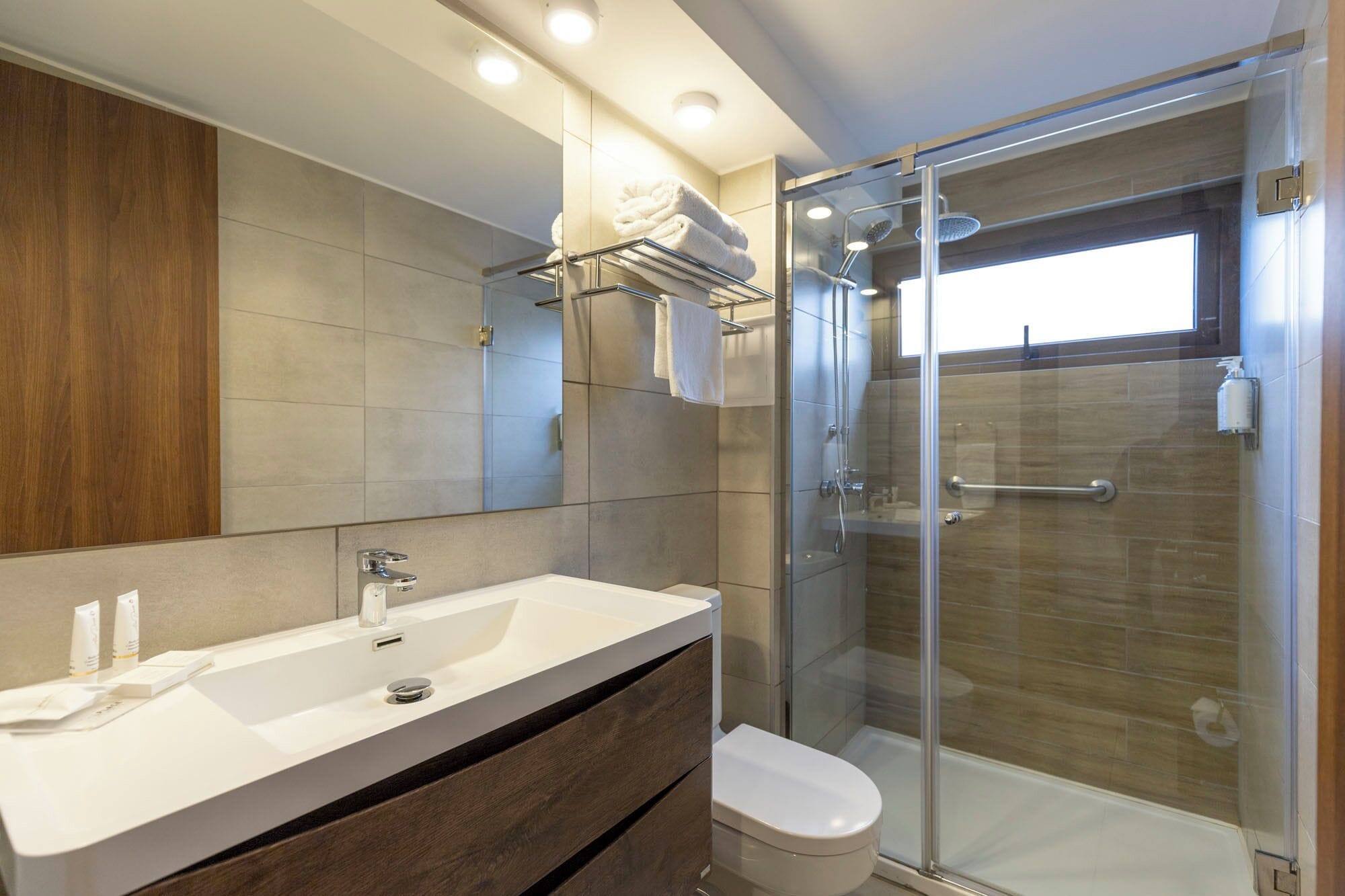 Une salle de bain moderne avec un grand miroir, un lavabo blanc, une douche en verre et des toilettes.