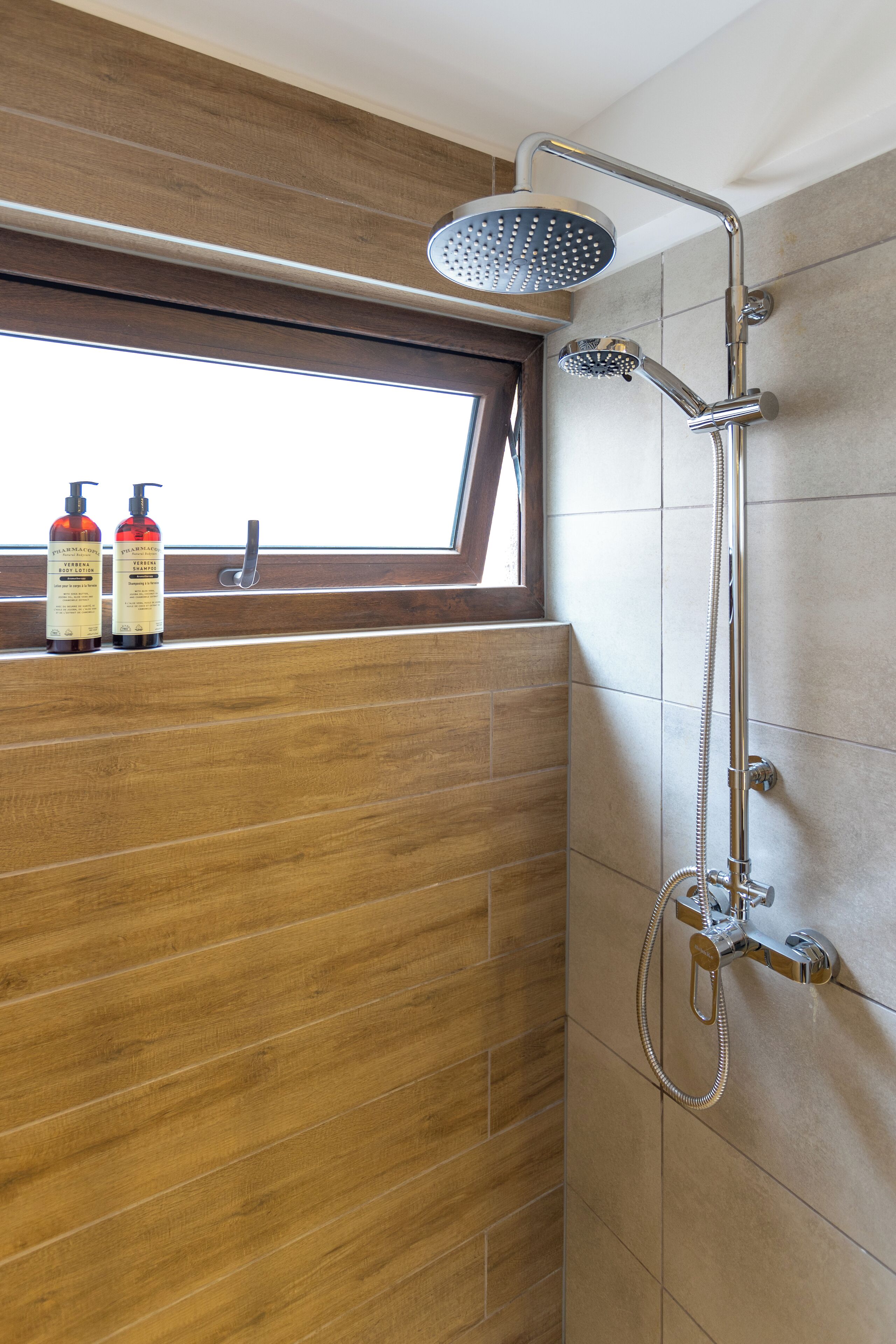 Ducha con cabezal de ducha de mano y grifo de pared. Hay dos botellas de champú sobre un repisa.