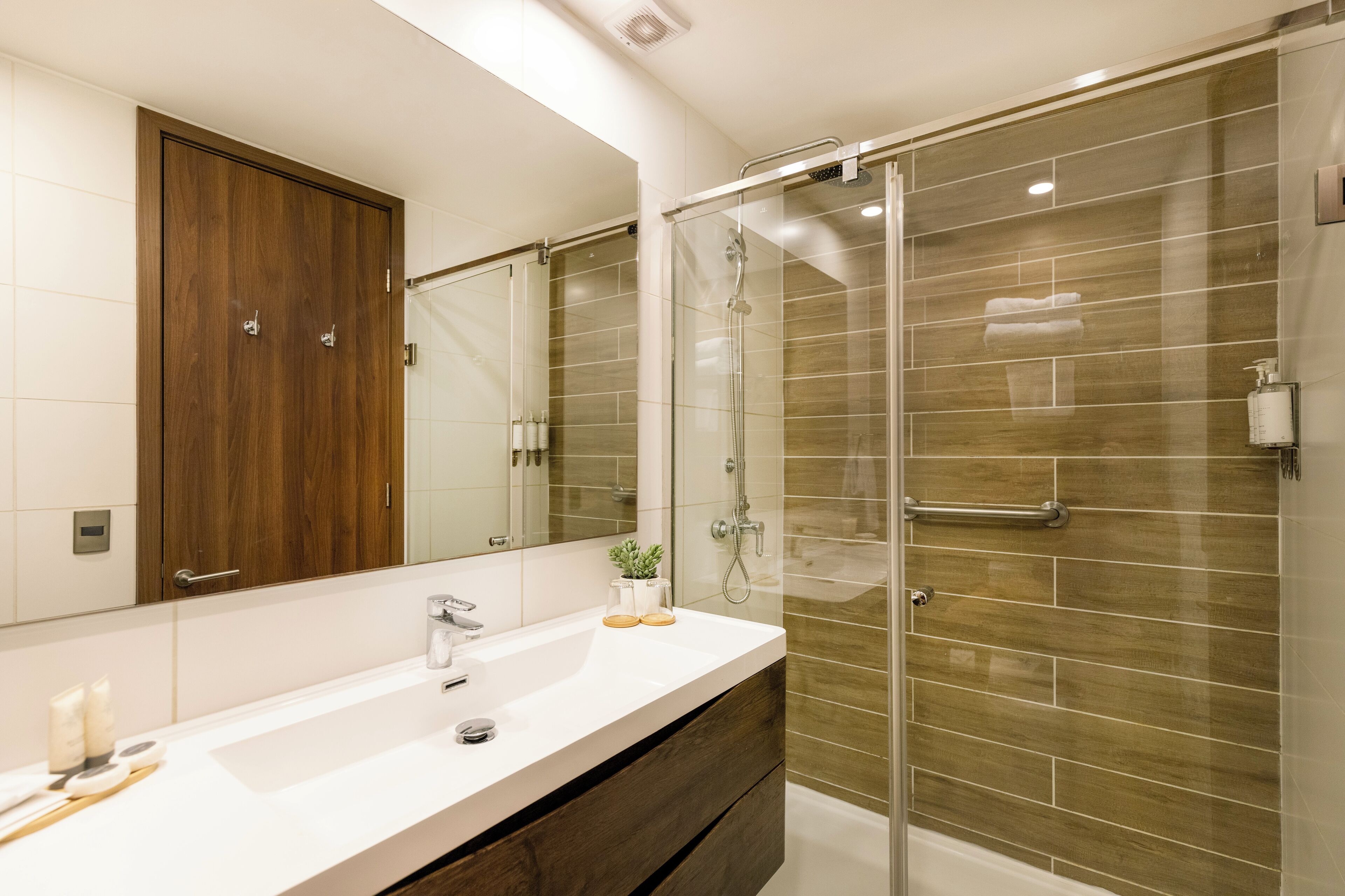 A modern bathroom with a large mirror, a white sink, a wooden vanity, and a glass-enclosed shower area.