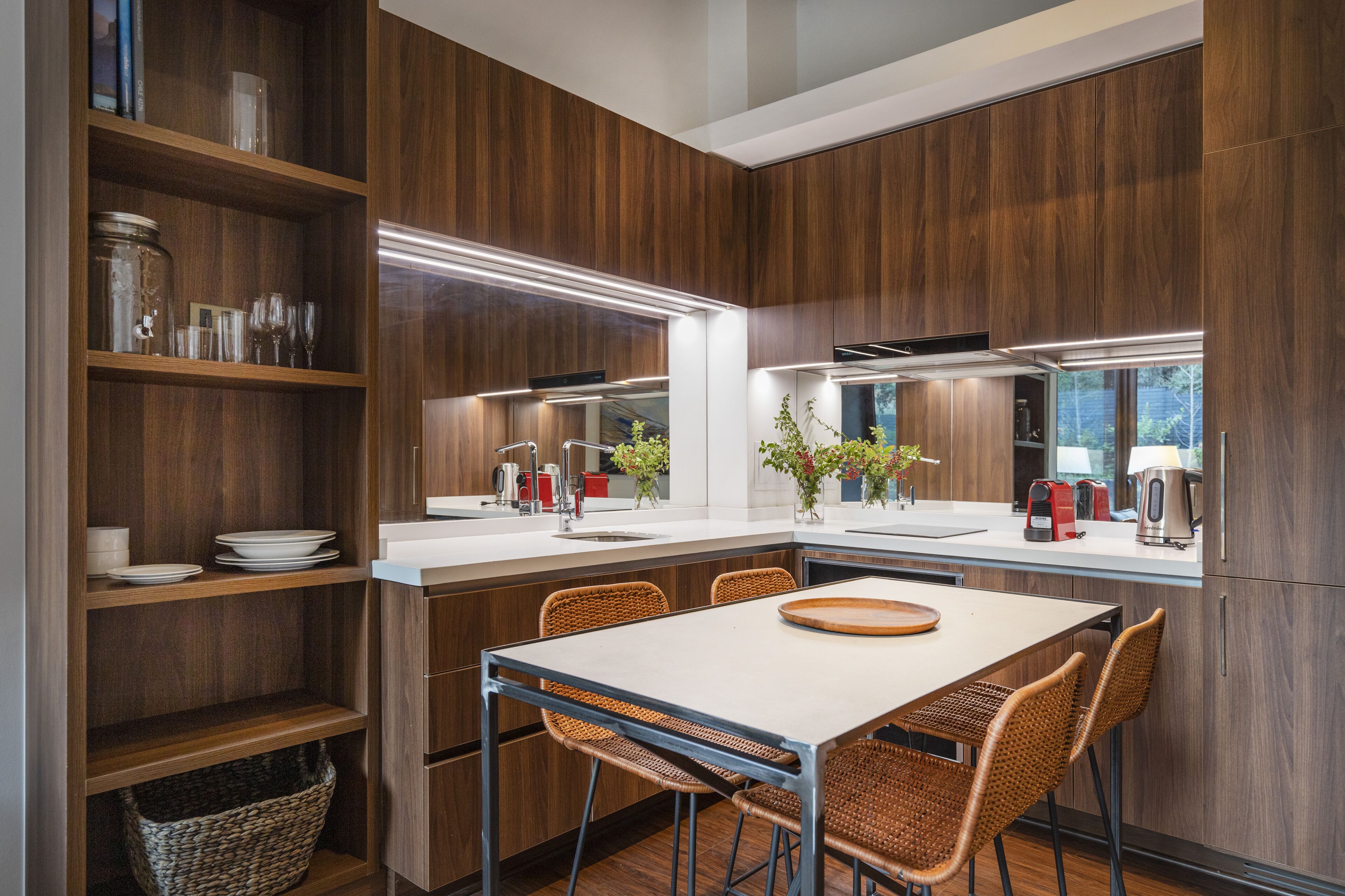 A modern kitchen with wooden cabinetry, a white countertop, and a dining area with wicker chairs.