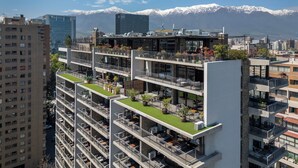 Um edifício moderno de vários andares com varandas, um jardim no terraço e vista para montanhas nevadas.