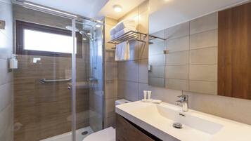 Un baño moderno con ducha envuelta en cristal, un lavabo blanco y un mueble de tocador de madera.