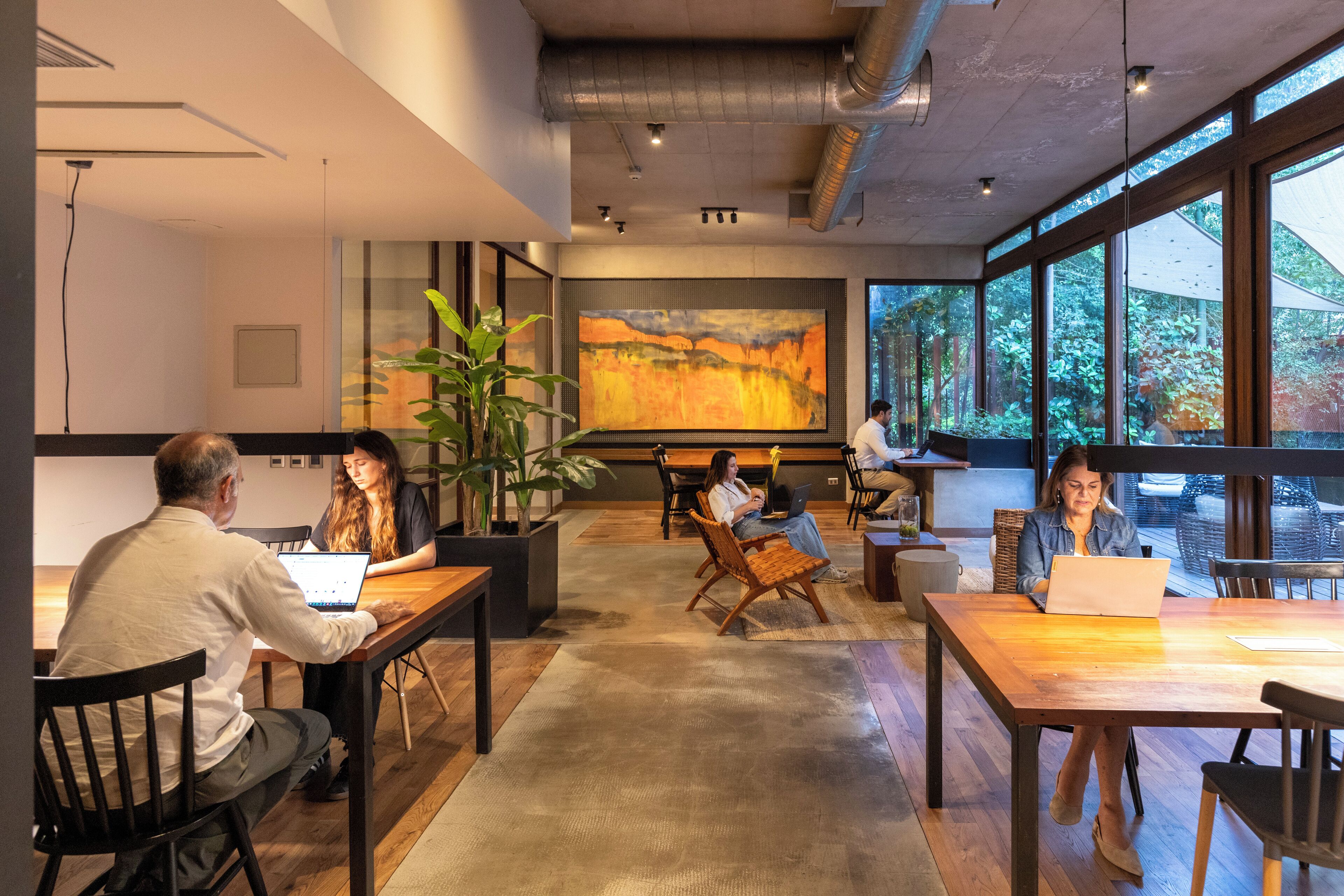 Une salle de réunion moderne, dotée de grandes fenêtres, d’un grand tableau abstrait et de plusieurs personnes travaillant à des tables.