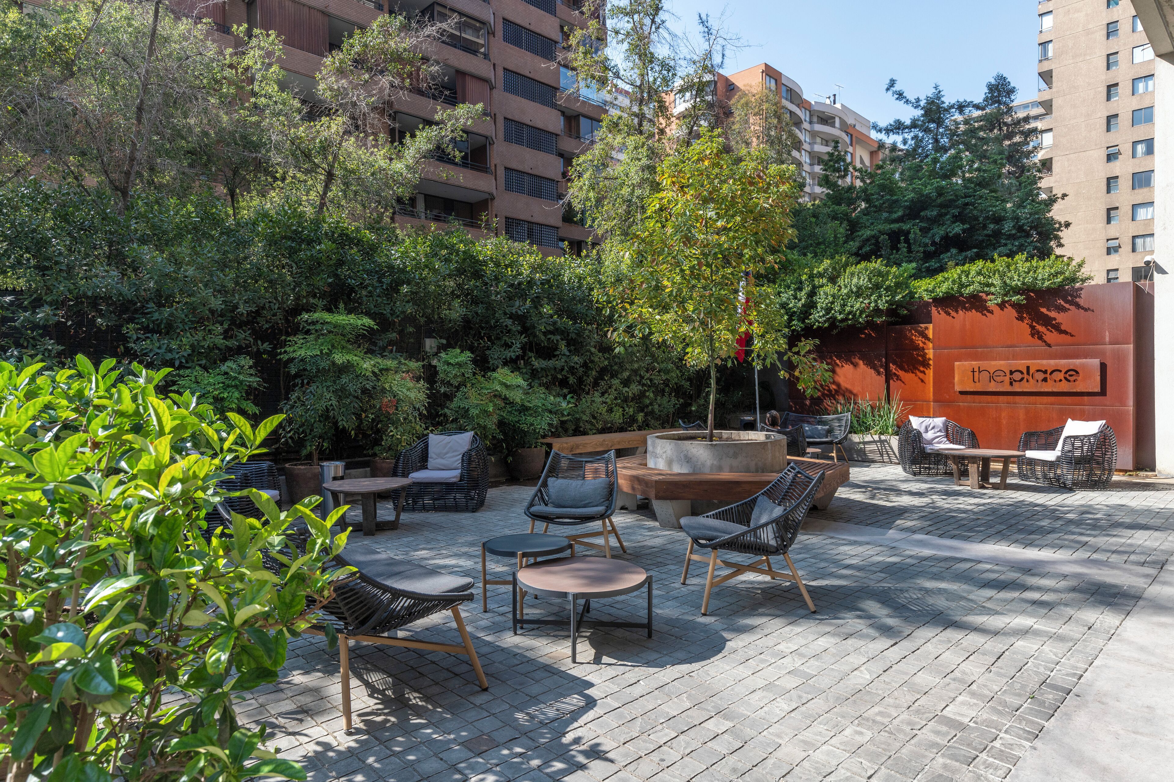 Un espace extérieur aménagé en terrasse, avec des sièges et de la verdure, une enseigne indiquant « theplace », et un bâtiment moderne en arrière-plan.