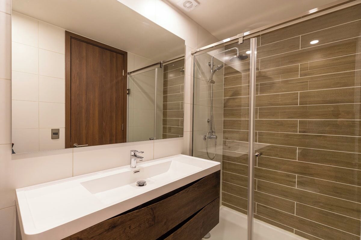 A modern bathroom with a white sink, a large mirror, and a glass-enclosed shower.